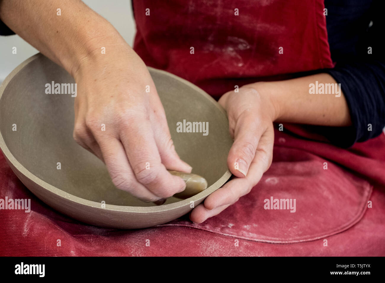 Close up of ceramic artist wearing red apron working on clay bowl. Stock Photo