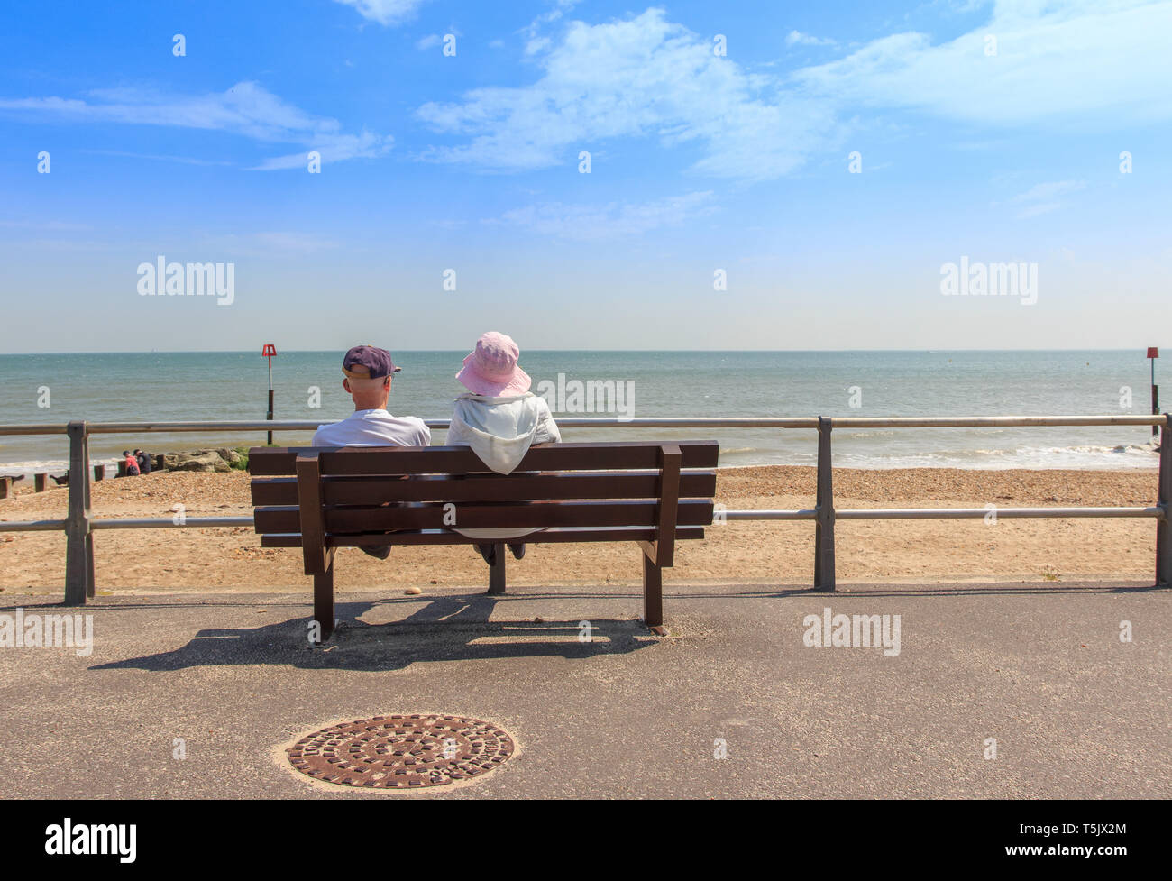 Elderly couple sitting on a bench looking out to sea at Avon Beach, Mudeford, Christchurch, Dorset UK Stock Photo