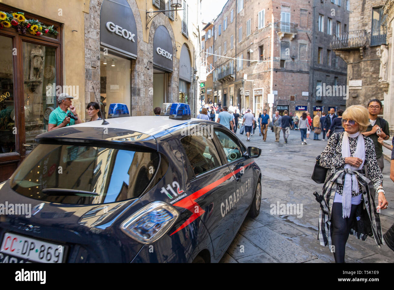 Carabineri police car drives past a glamorous italian woman in the narrow streets of Siena,Tuscany,Italy Stock Photo