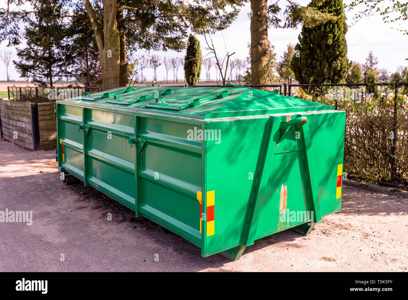 A large, metal, green garbage container and municipal waste, standing on a  dirt road near the fence and trees Stock Photo - Alamy