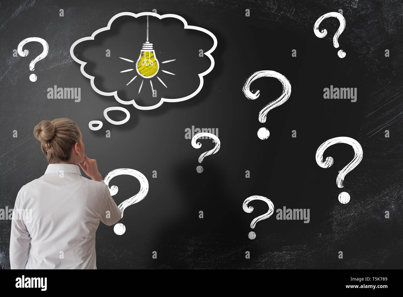 finding solution to problem or answer to question concept with woman looking at chalkboard with question marks while having an idea Stock Photo