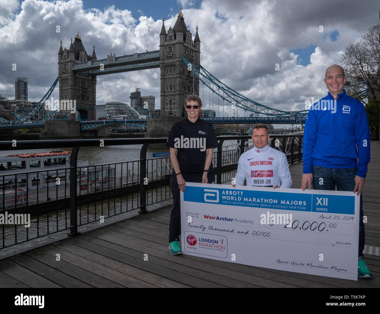David Weir flanked by Michelle Weltman, Elite Wheelchair Coordinator, Abbot World Marathon Majors and Chris Miller DVP, Global Brand Strategy & Innovation, Abbott accepts a cheque on behalf of the Weir Archer Academy from Abbot World Marathon Majors for £20,000 to mark his 20th consecutive London Marathon during a photocall outside Tower Bridge, London. Stock Photo