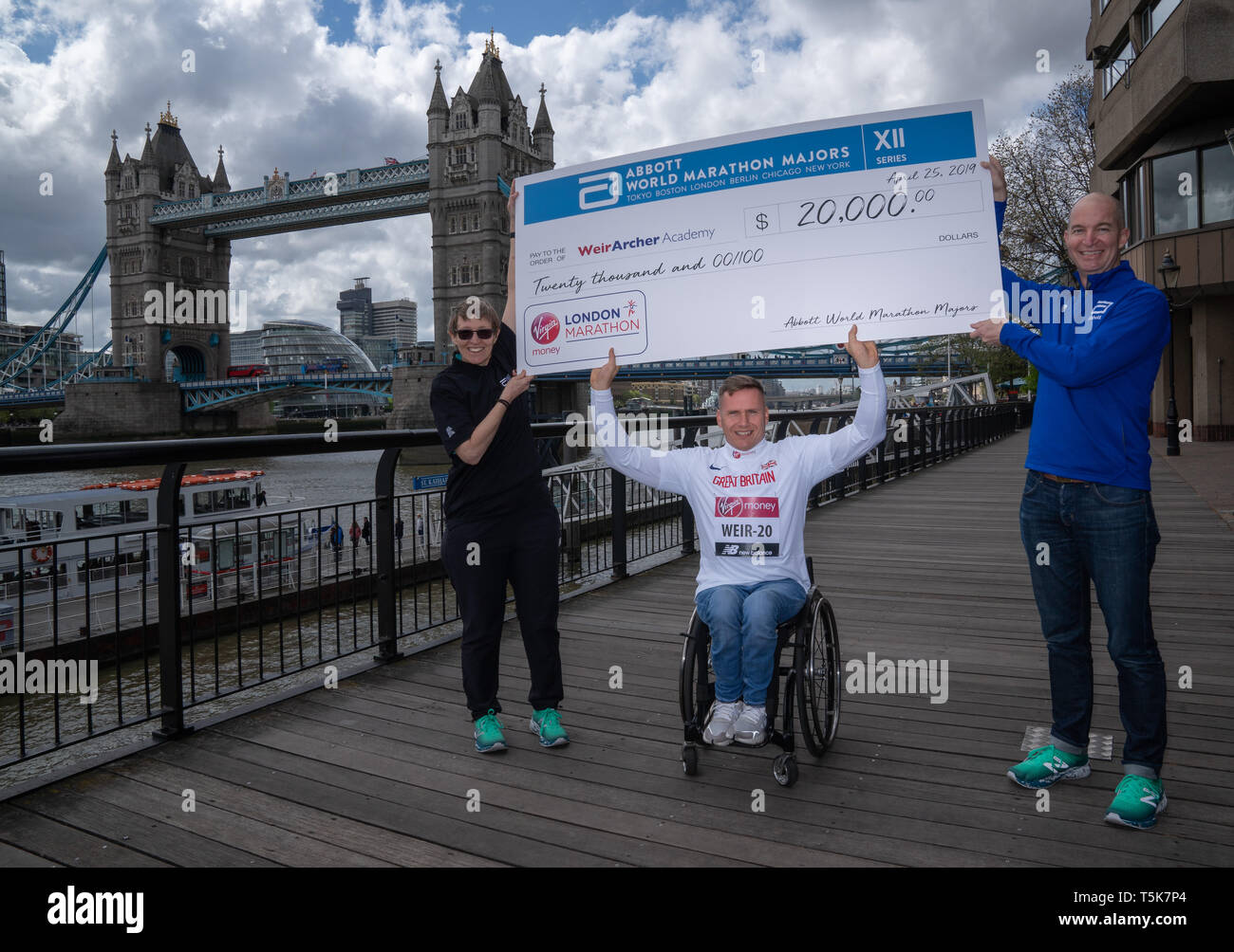 David Weir flanked by Michelle Weltman, Elite Wheelchair Coordinator, Abbot World Marathon Majors and Chris Miller DVP, Global Brand Strategy & Innovation, Abbott accepts a cheque on behalf of the Weir Archer Academy from Abbot World Marathon Majors for £20,000 to mark his 20th consecutive London Marathon during a photocall outside Tower Bridge, London. Stock Photo