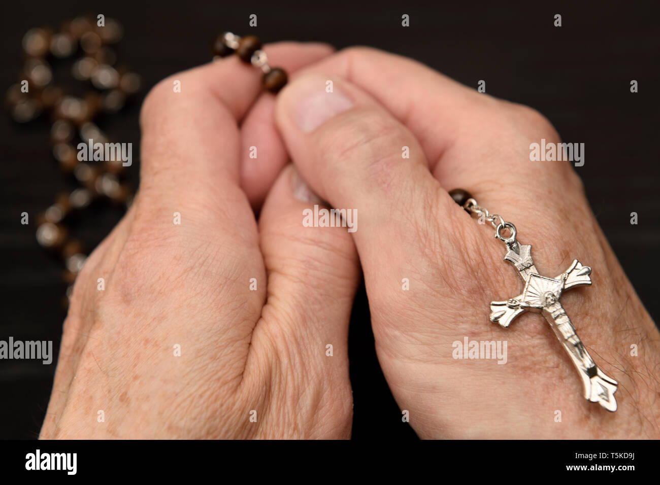 Hands of old man meditating and praying on the beads of a rosary with crucifix Stock Photo