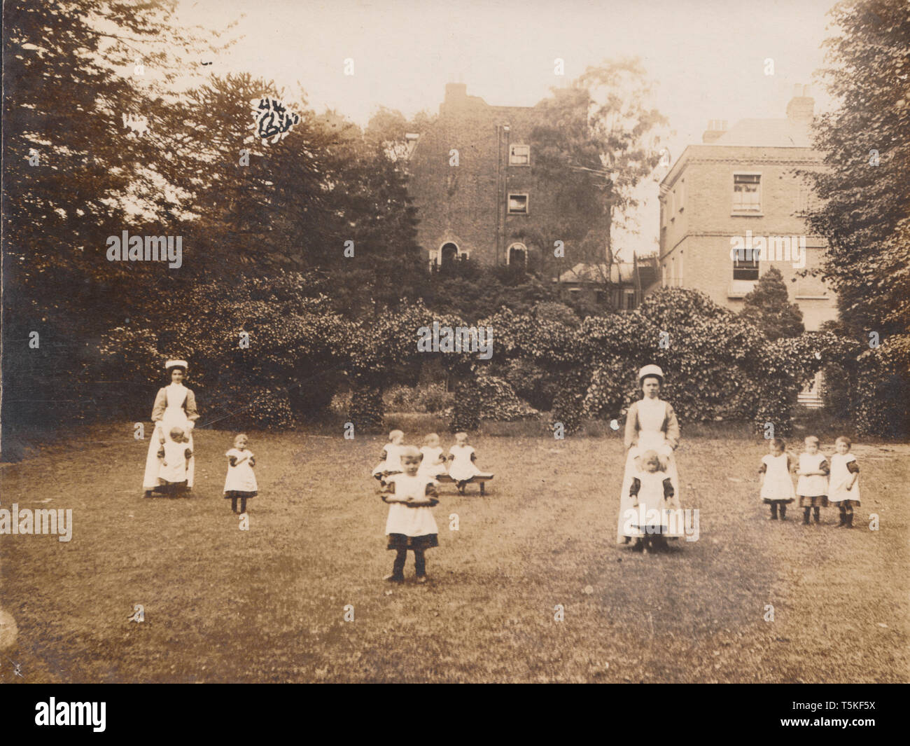 Vintage Photographic Postcard of a Chidren's Orphanage Possibly Called Percy House. Nurses and Children Enjoying Time in The Garden. Stock Photo