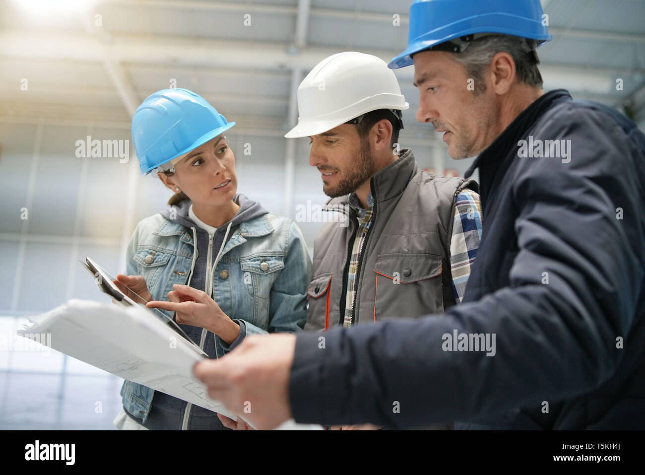 Team of construction workers talking in empty warehouse Stock Photo