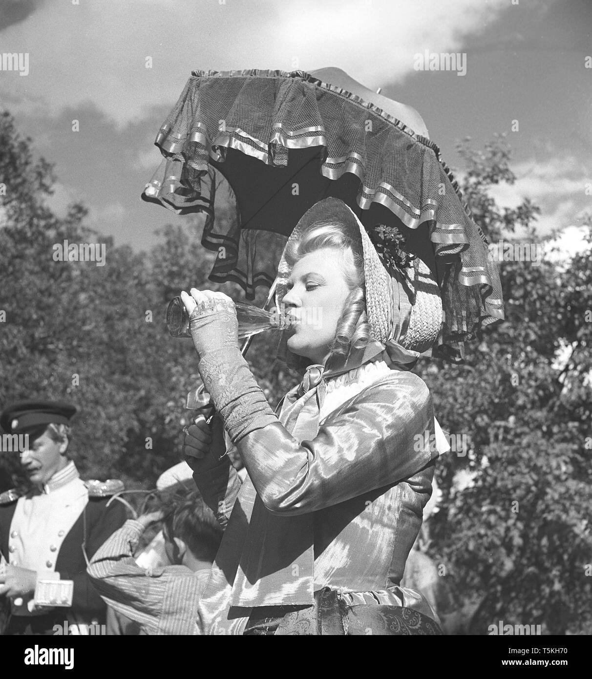 1940s actress. A young woman on a movie set dressed in historical clothing is cooling down by drinking from a bottle. Photo Kristoffersson ref V48-6. Sweden 1947 Stock Photo