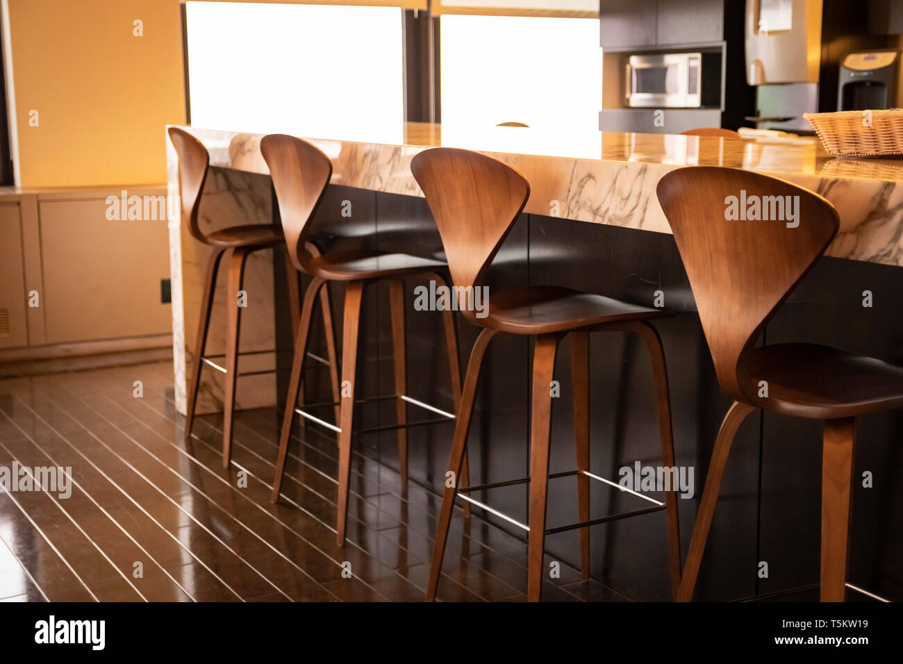 Fine wood chairs lined up at a spacious kitchen breakfast bar Stock Photo