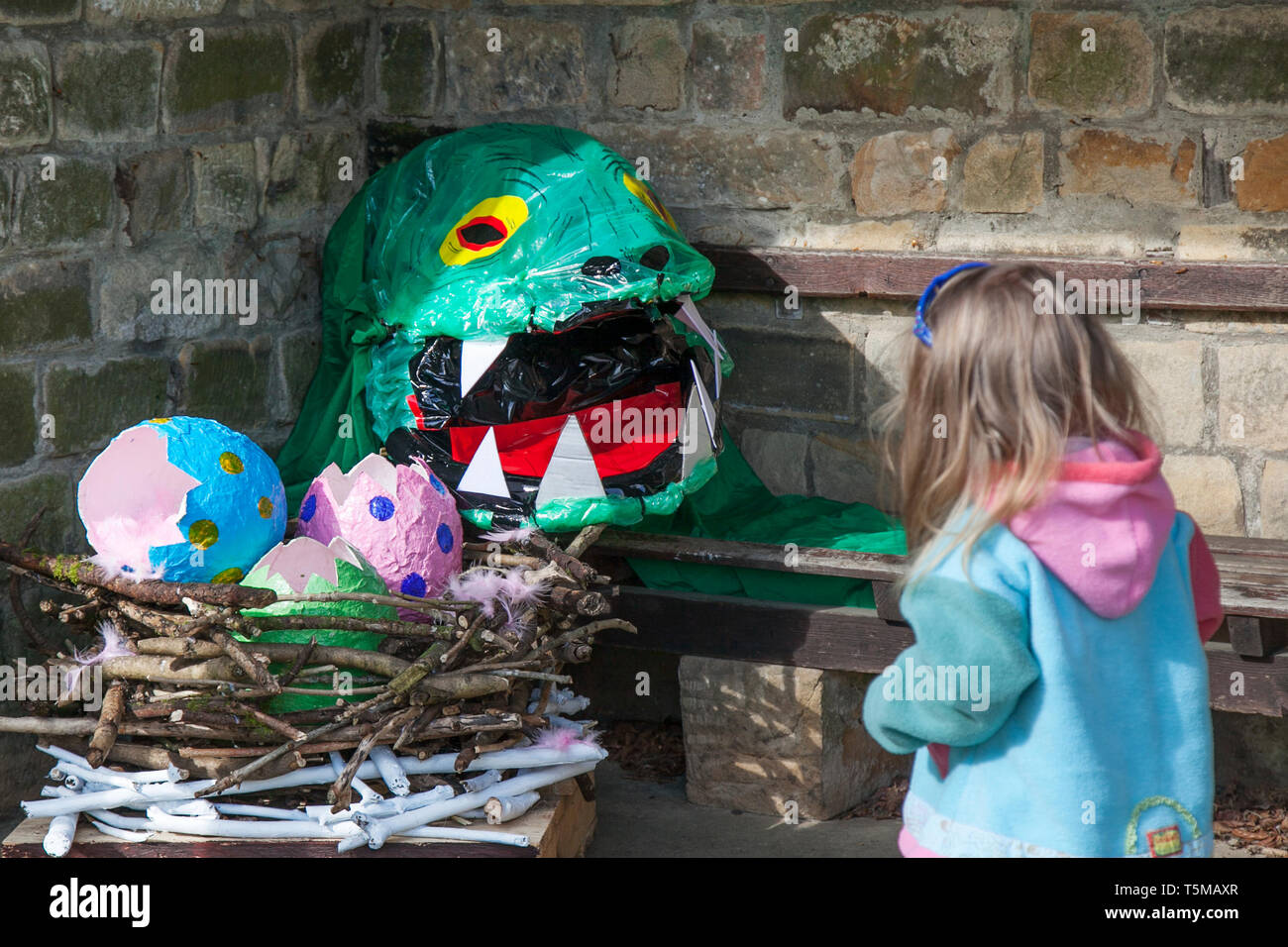 Open mouthed dinosaurs with paper mache chicks at the Wray Scarecrow Festival parade established 1995. This quirky even takes place every year, with a different theme in the week leading up to May Day.  Villagers put up weird, wacky, unusual, wonderful funny straw stuffed scarecrow creations to attract visitors. Stock Photo