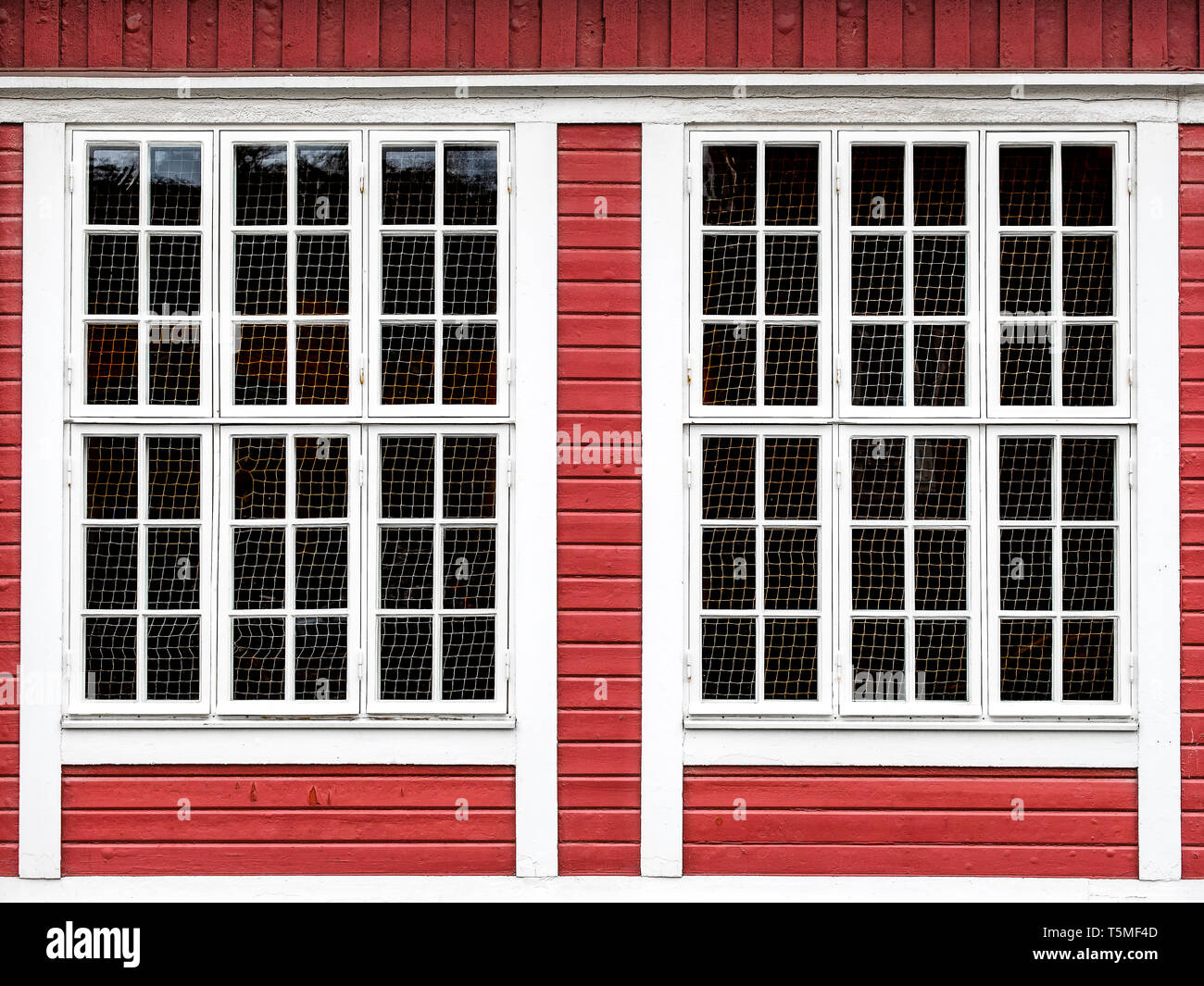 Big windows on a red wooden wall, with white framing along the windows. Stock Photo