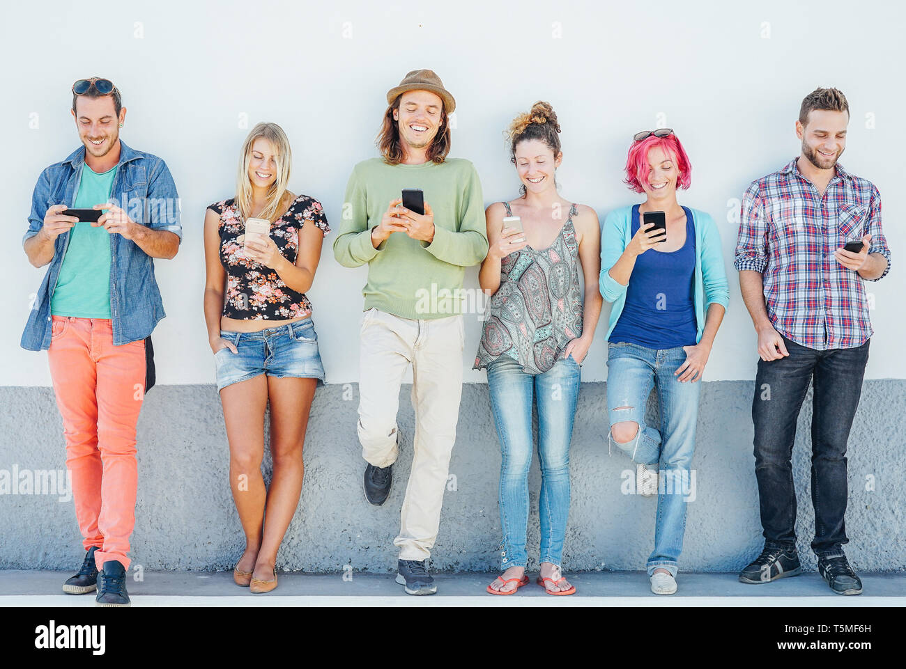 Young people watching on their smart mobile phones leaning on a wall - Generation addicted to new technology Stock Photo