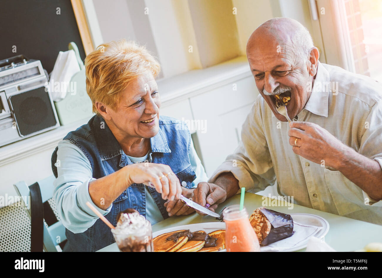 Happy seniors couple eating pancakes in a bar restaurant - Mature people having fun dining together at home - Concept of elderly lifestyle moments Stock Photo