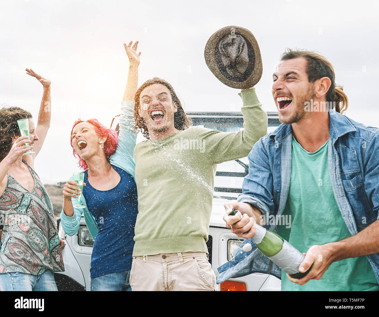 Group of happy friends making party with a bottle of champagne - Travel people having fun celebrating during their road trip with convertible car Stock Photo
