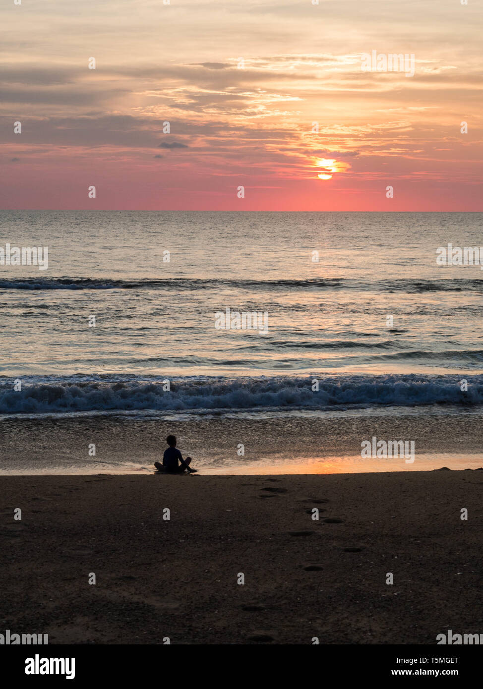 Silhouette of an indefinite person in lotus position on a sea sandy beach during a beautiful sunset. Meditation during sunset. A child is meditating o Stock Photo