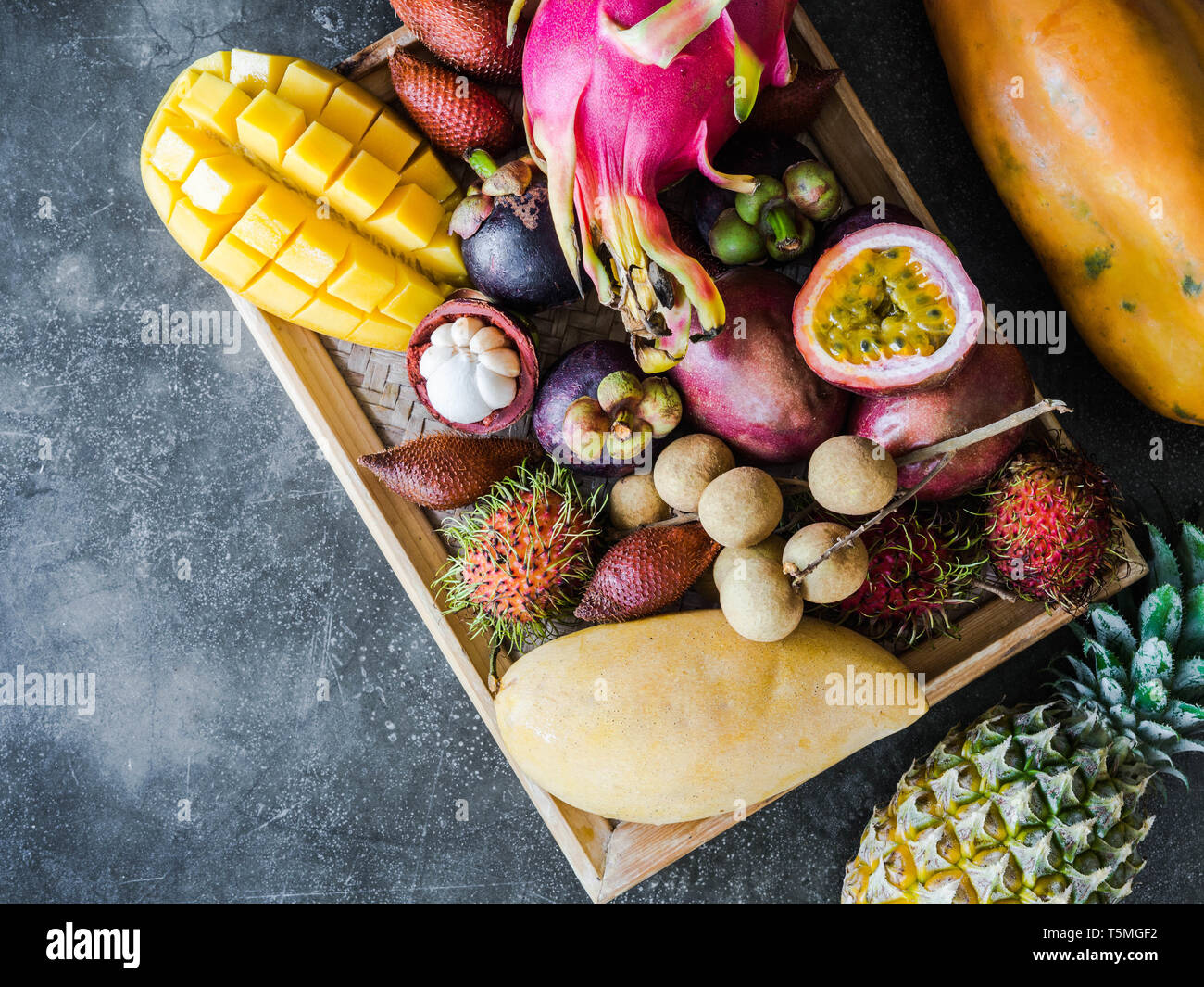 Various fresh Thai fruits - rambutan, mango, mangosteen, longan, papaya, dragon fruit, sapodilla, passion fruit, salak, pineapple on a wooden tray and Stock Photo
