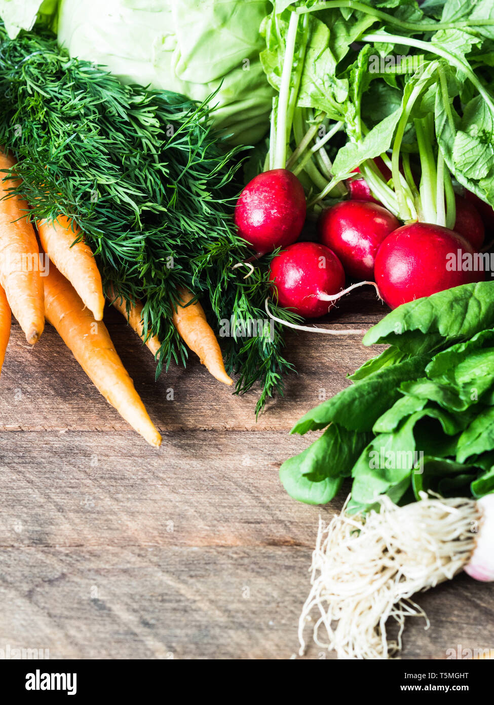 Fresh Spring vegetables and herbs - carrots, ramson, radish, dill, garlic, cabbage on a wood background. Spring harvest of fresh vegetables. Stock Photo