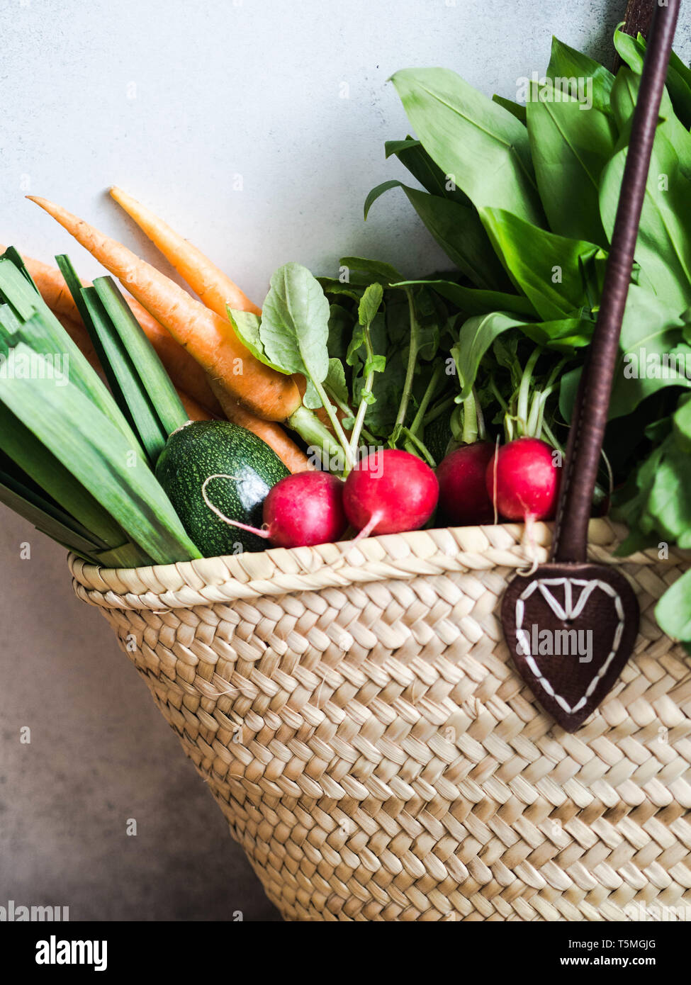 Wicker straw bag full of fresh natural spring vegetables. Healthy vegetarian vegan food from the local market from farms Stock Photo