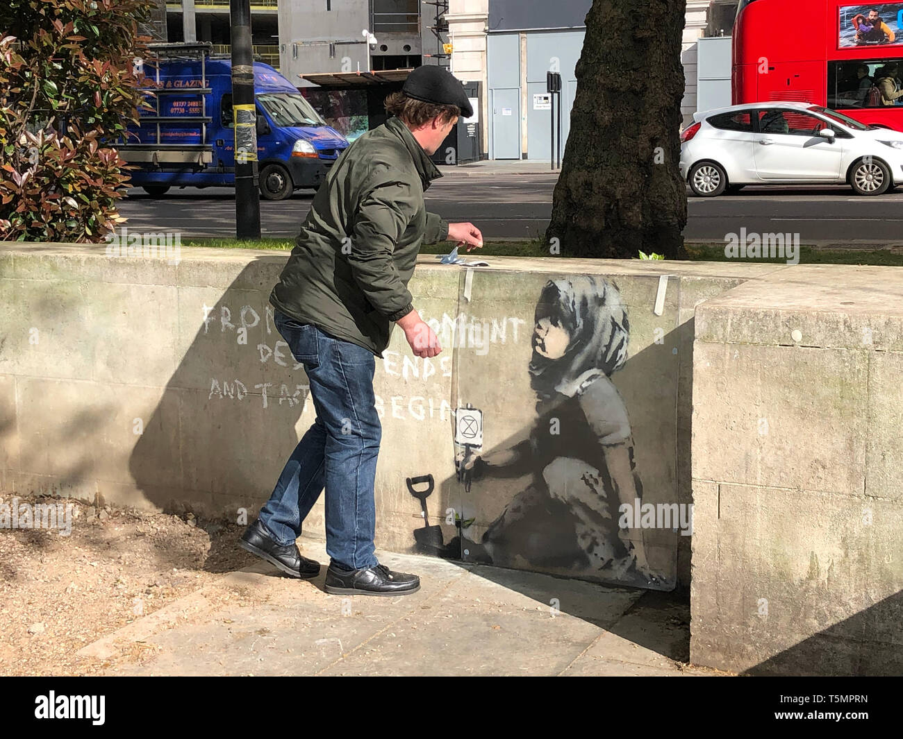 Calvin Benson, 48, puts a protective plastic sheeting over an artwork which appears to be by street artist Banksy. The environmental artwork has appeared near the Extinction Rebellion camp in Marble Arch, London. Stock Photo