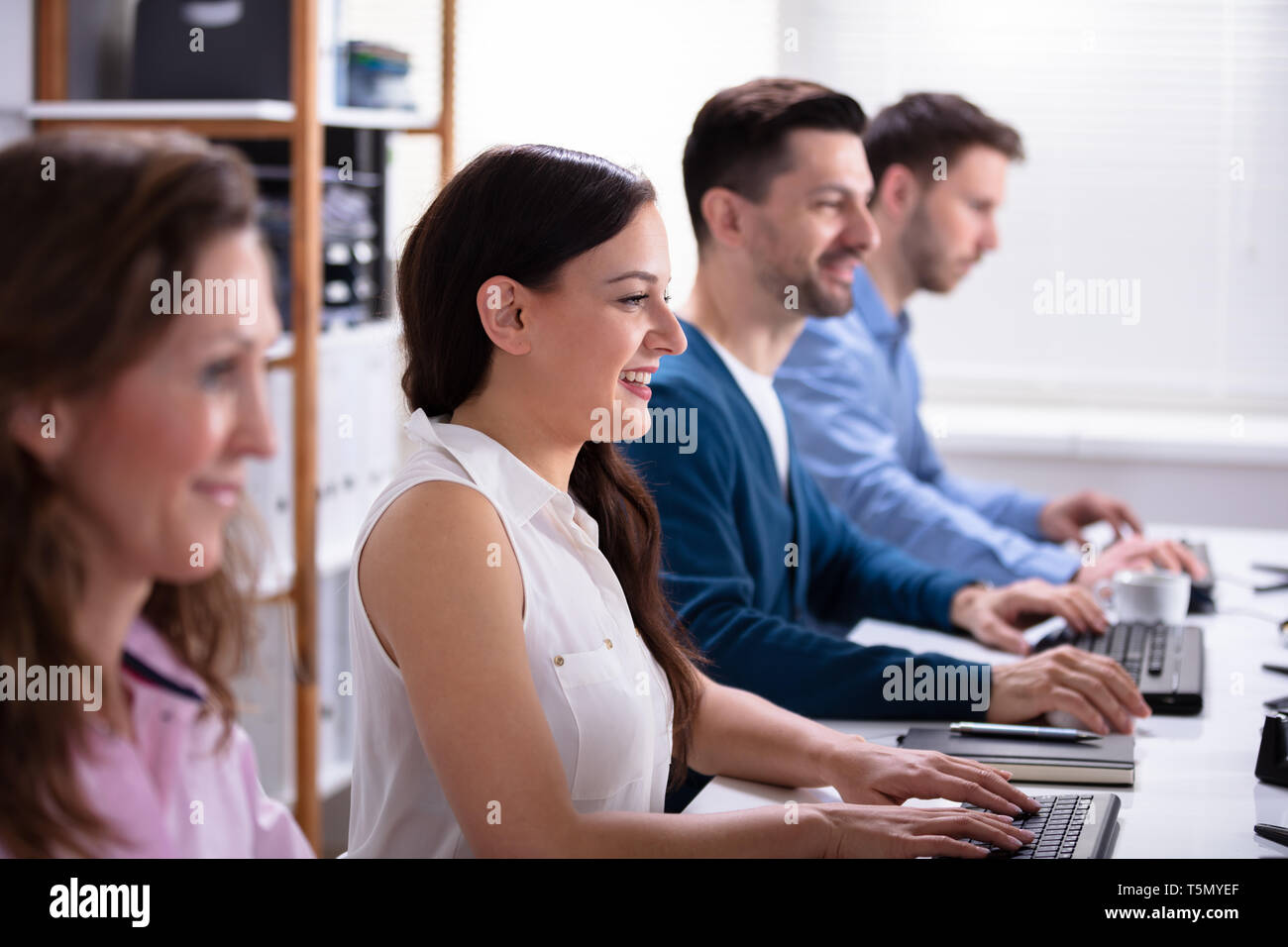 Smiling Young Business People Sitting In A Row Using Computer Stock Photo