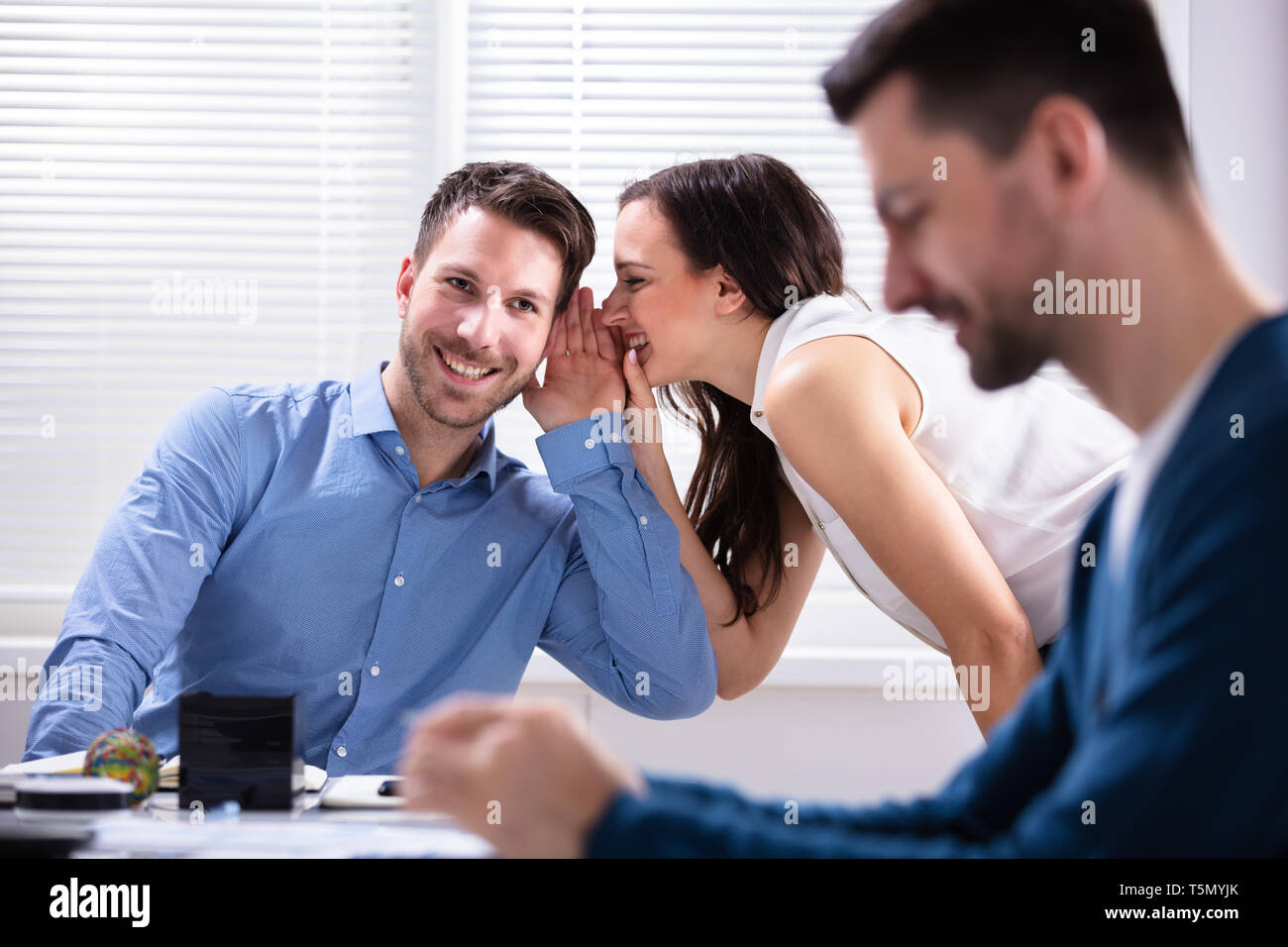 Smiling Young Two Businesspeople Gossiping About Their Colleague In Office Stock Photo