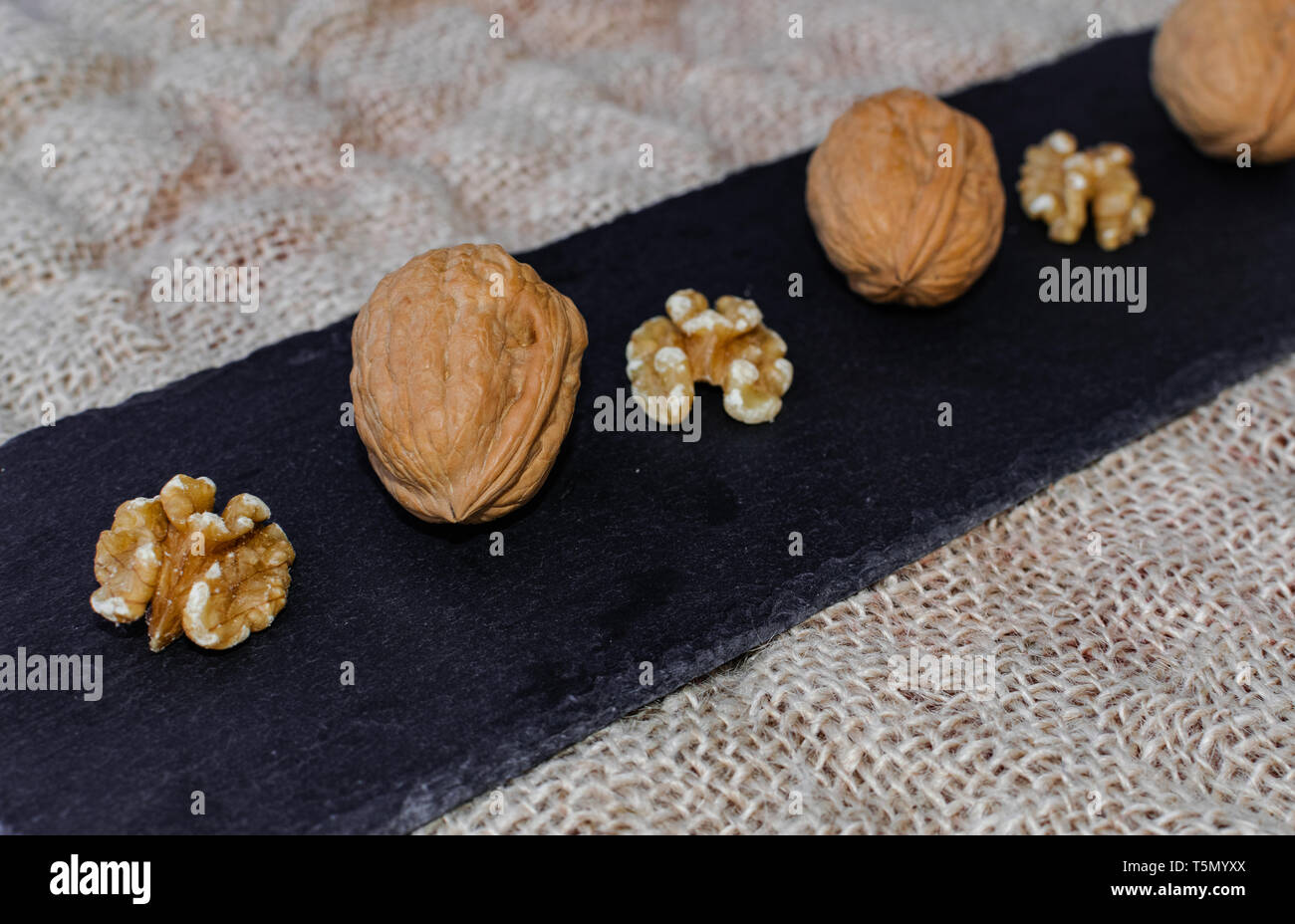 Walnuts, with and without shell, on black table surface, over sack texture Stock Photo