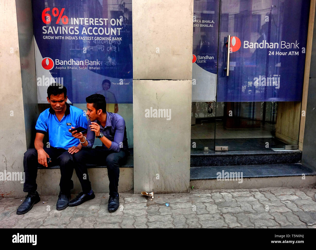 Two men are seen seated in front of the Bandhan Bank branch office in