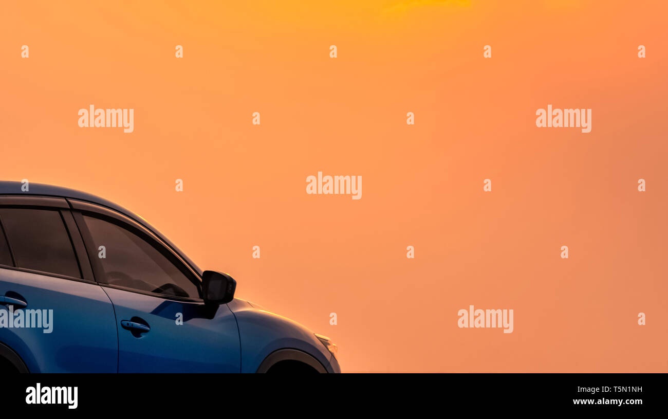 Blue compact SUV car with sport and modern design parked by the sea with beautiful orange sunset sky. Road trip travel. Electric car technology Stock Photo