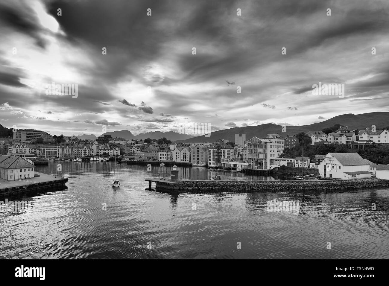 Moody Black And White Photo Of A Small Sailing Boat Entering The Picturesque Harbour In Ålesund, Møre og Romsdal, Norway. Stock Photo