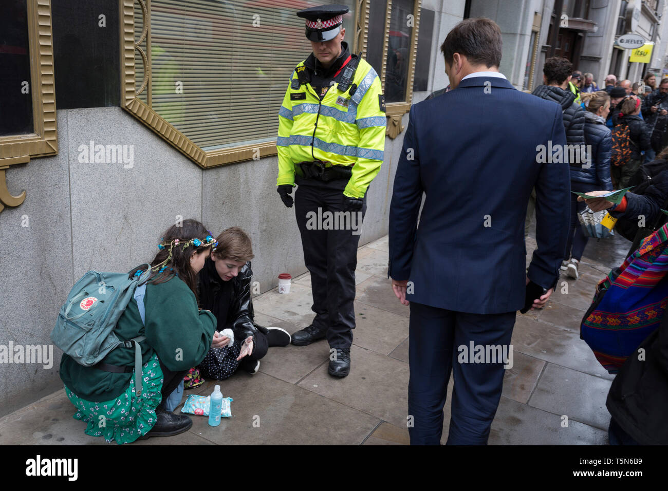 A police officer watches over an environmental protester with Superglue on her hands after glueing body parts to the road in Fleet Street on the 11th and final day of protests, road-blockages and arrests across London by the climate change campaign Extinction Rebellion, on 25th April 2019, in London, England. Stock Photo