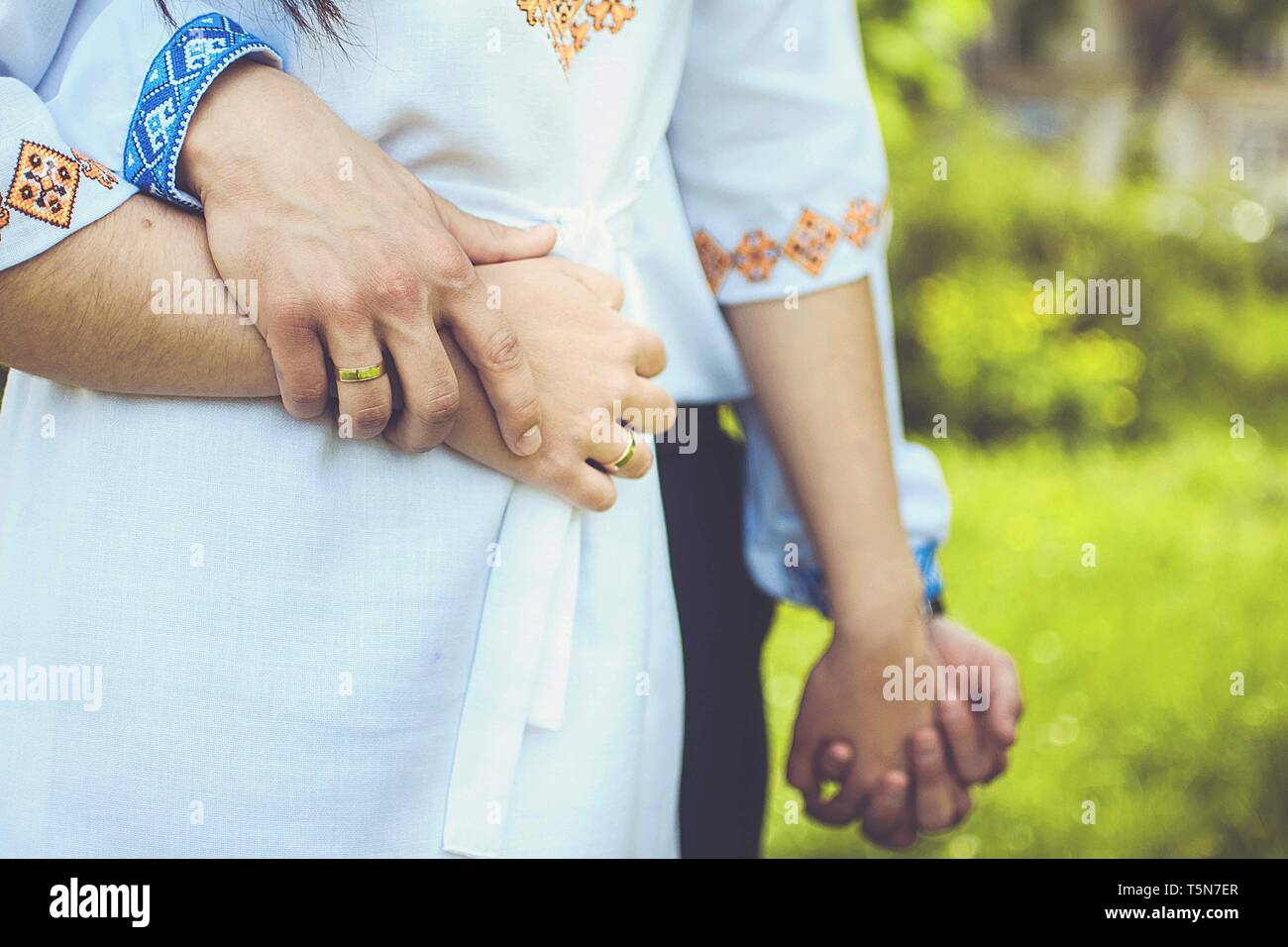 Man hugs woman and holding hand in ukrainian traditional clothes. Embroidered clothes by blue and yellow colors. Stock Photo