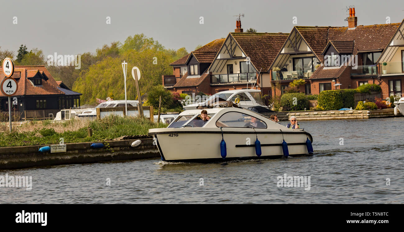 Family on a small hire boat navigating the River Bure in Horning, a village in the heart of the