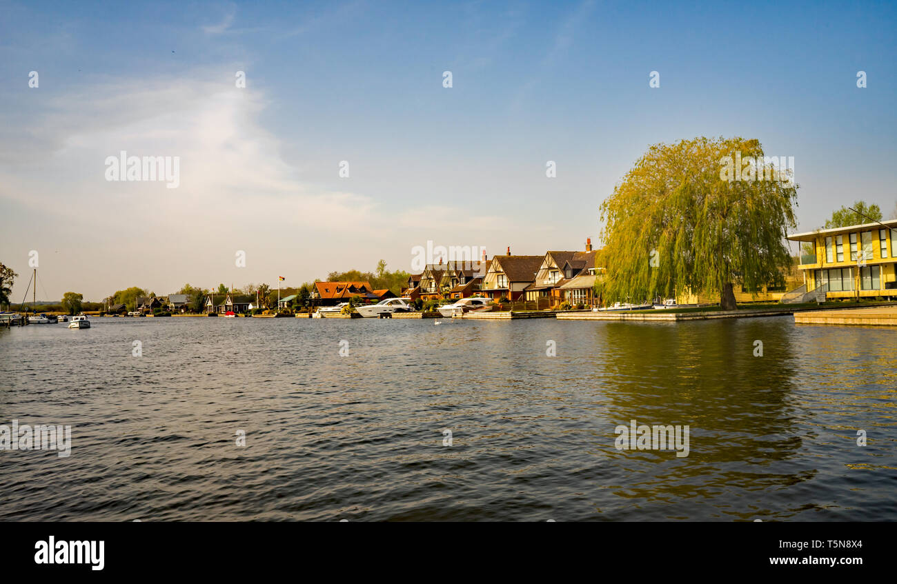 A view up the River Bure from the bank of the public riverside park in the village of Horning, Norfolk. A small day boat is heading south whilst passi Stock Photo