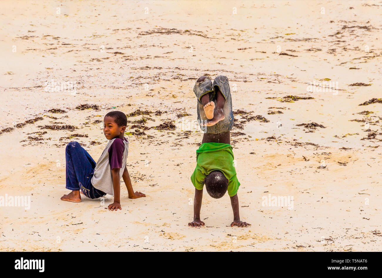 Zanzibar, Tanzania, March 21, 2018. Two small african children in in the sand in tattered  smutty clothes playing for money in sunny day Stock Photo