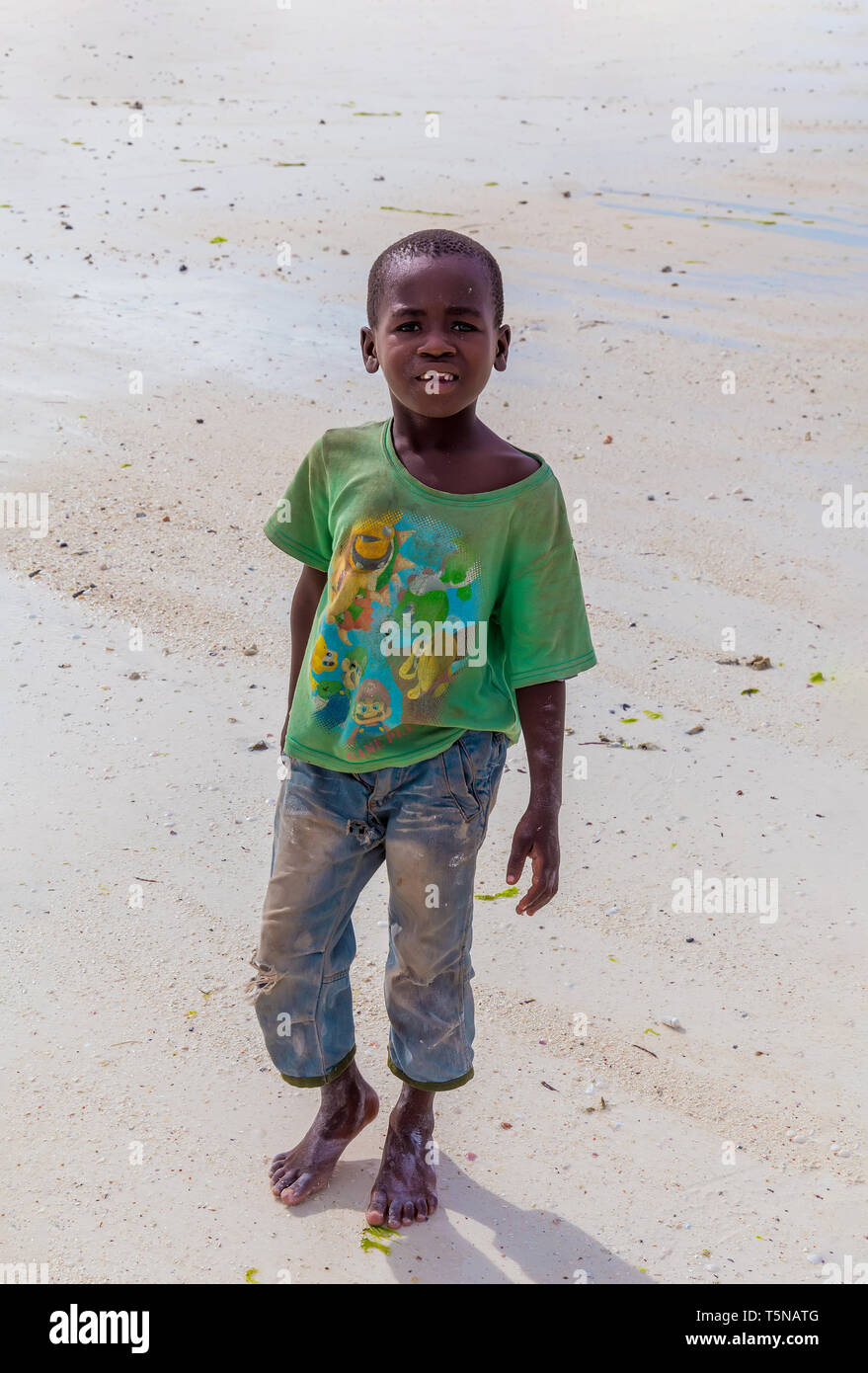 Tanzania, Zanzibar, march 21, 2018. One small african boy stands barefoot on sand in torn and dirty clothes. Stock Photo