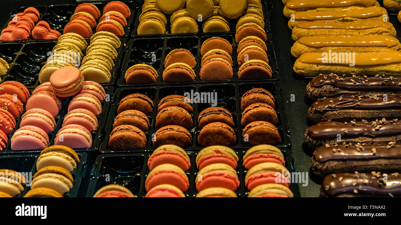 Many colorful makaroons and chocolate and caramel eclair with nuts and cream on display Stock Photo