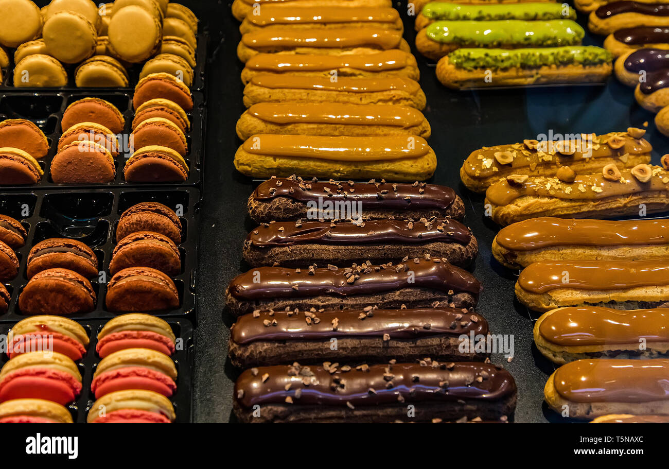 Many colorful makaroons and chocolate and caramel eclair with nuts and cream on display Stock Photo
