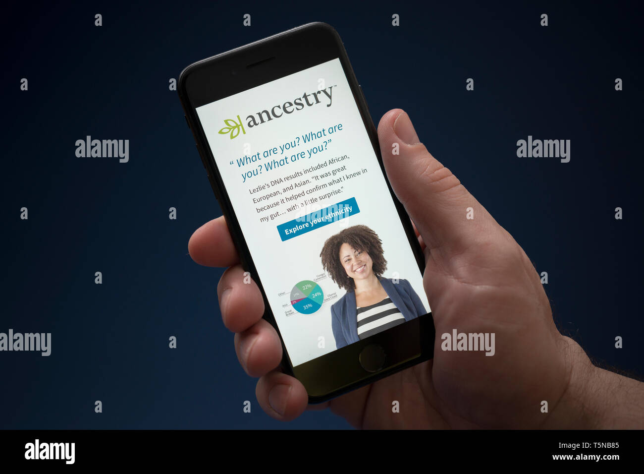 A man looks at his iPhone which displays the Ancestry logo (Editorial use only). Stock Photo