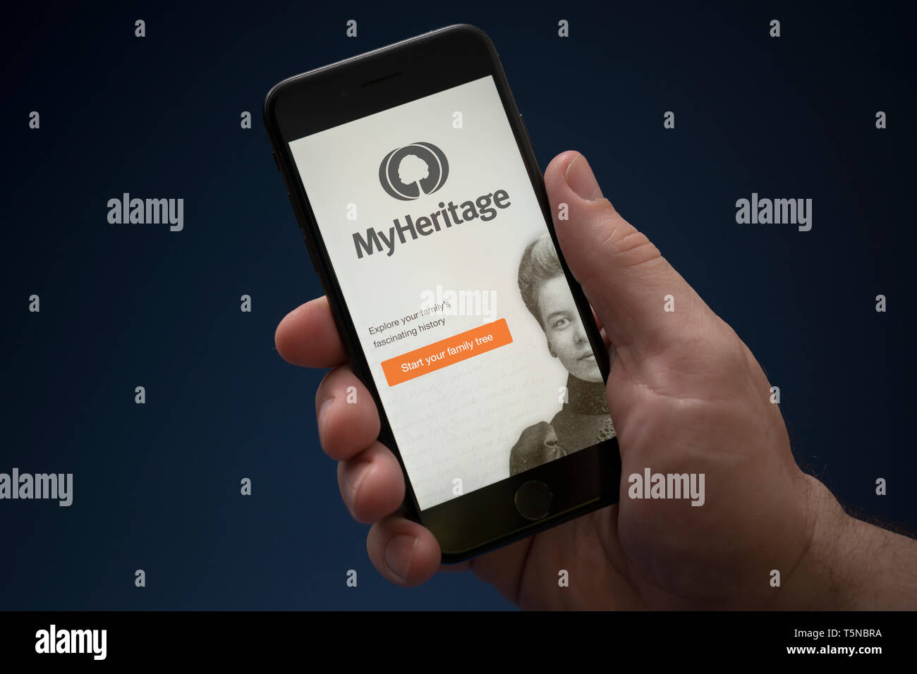 A man looks at his iPhone which displays the MyHeritage logo (Editorial use only). Stock Photo