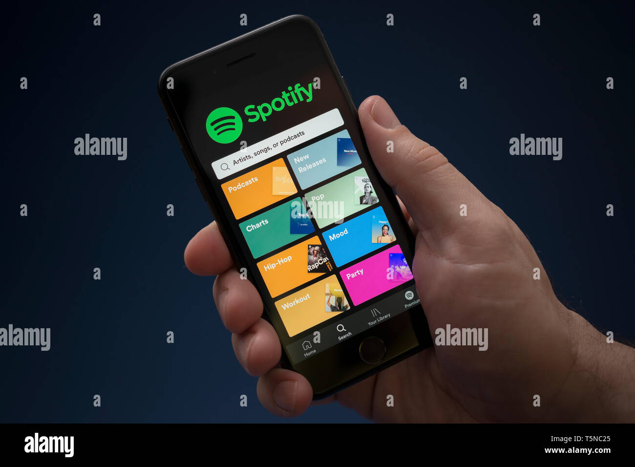 A man looks at his iPhone which displays the Spotify logo (Editorial use only). Stock Photo