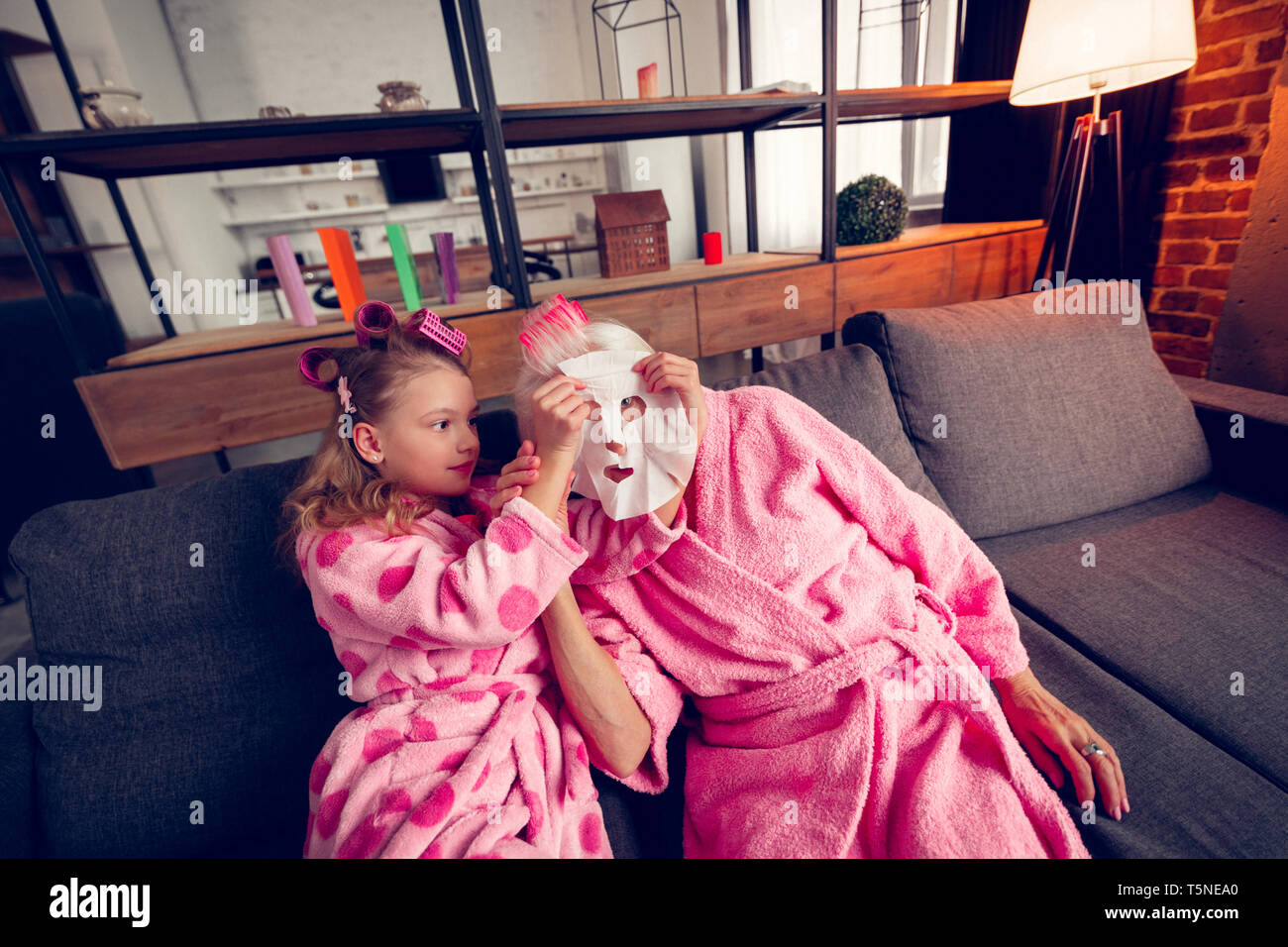 Caring cute girl putting moisturizing mask on face of granny Stock Photo