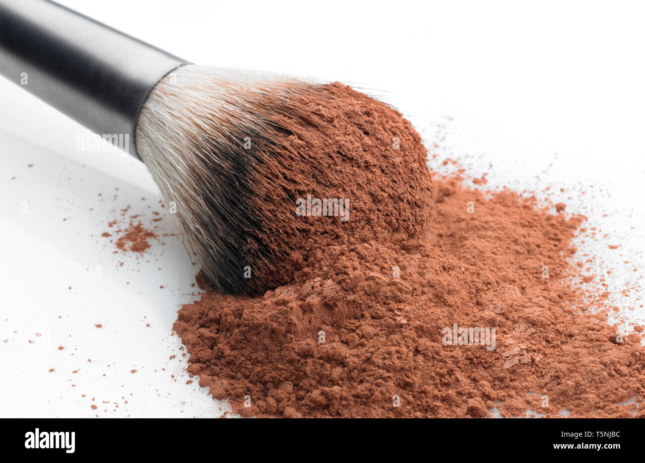 Shallow depth of focus. Close up view of a makeup brush over a pile of cosmetic compact powder. White background Stock Photo