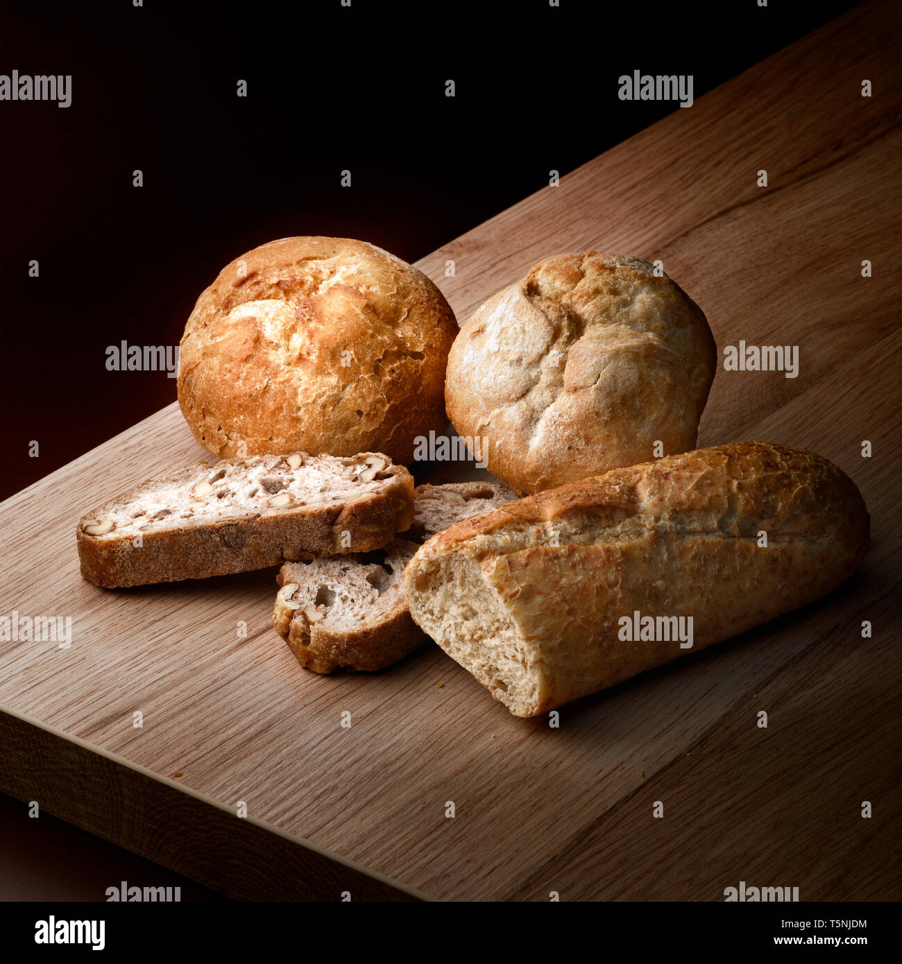 Arrangement of assortment of crunchy baked bread against wooden table in a dark ambiance Stock Photo