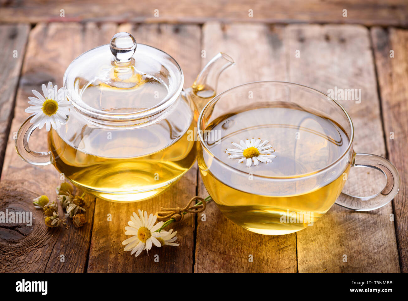 Glass of chamomile tea with full hot teapot with dried and fresh chamomile flowers on vintage ...