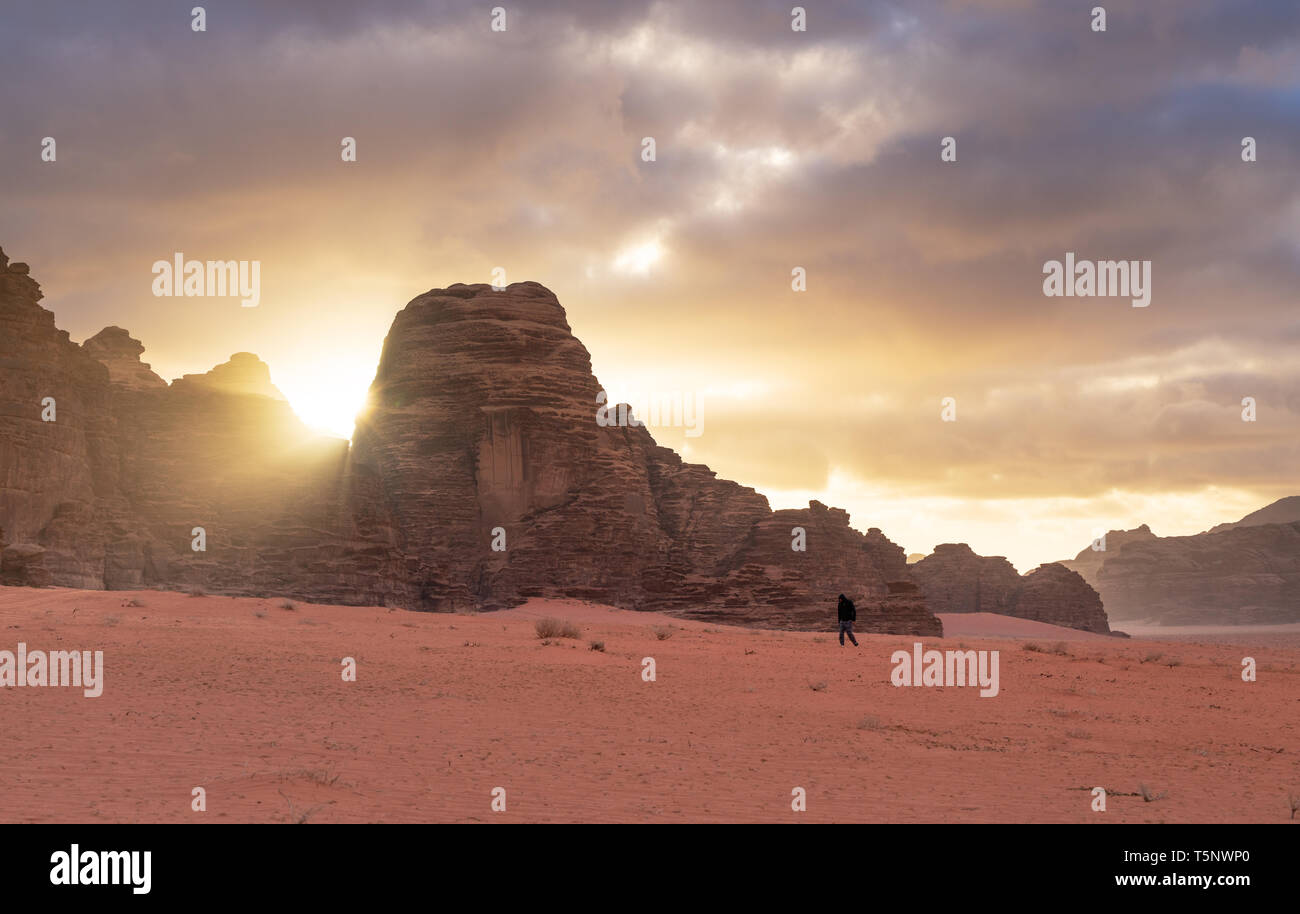 Landscape of Wadi Rum desert in sunrise with a man walking alone, and sunlight through stone mountain. Travelling and adventurous in desert, Jordan Stock Photo