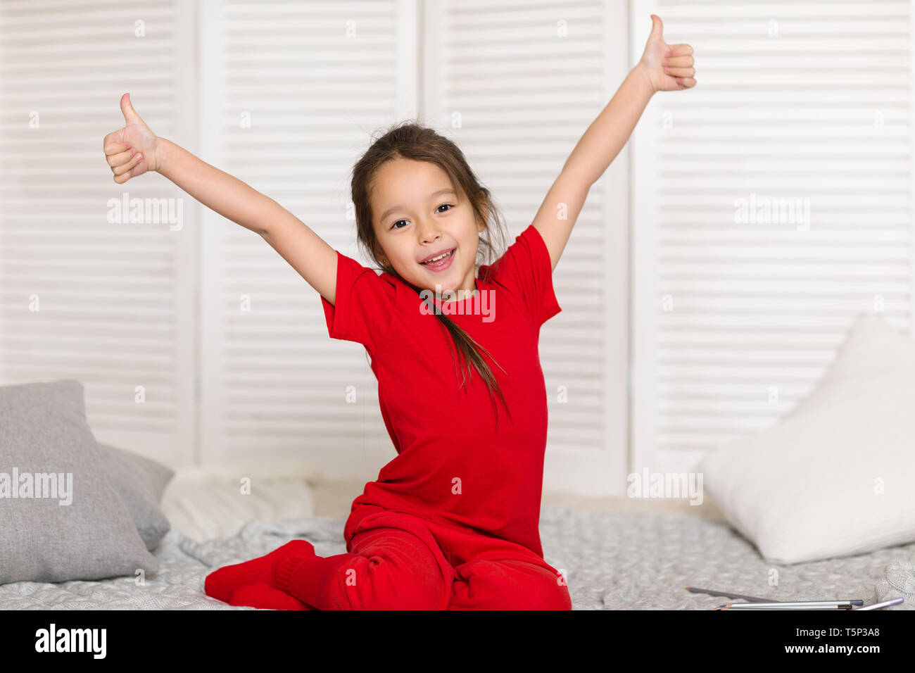 happy cute little child girl in red pajamas draws with pencils at home ...
