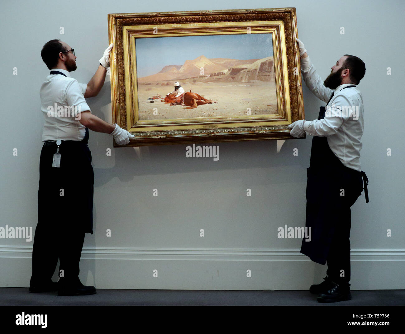 Two gallery technicians adjust Jean-Leon Gerome's work 'Rider and his Steed in the Desert' at a preview for the forthcoming Sotheby's Middle Eastern Art Week sale which takes place on the 30th April in London. Stock Photo