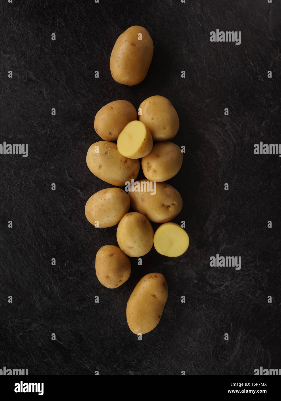 Raw potatoes on black textured background, dark food. Photo from above Stock Photo