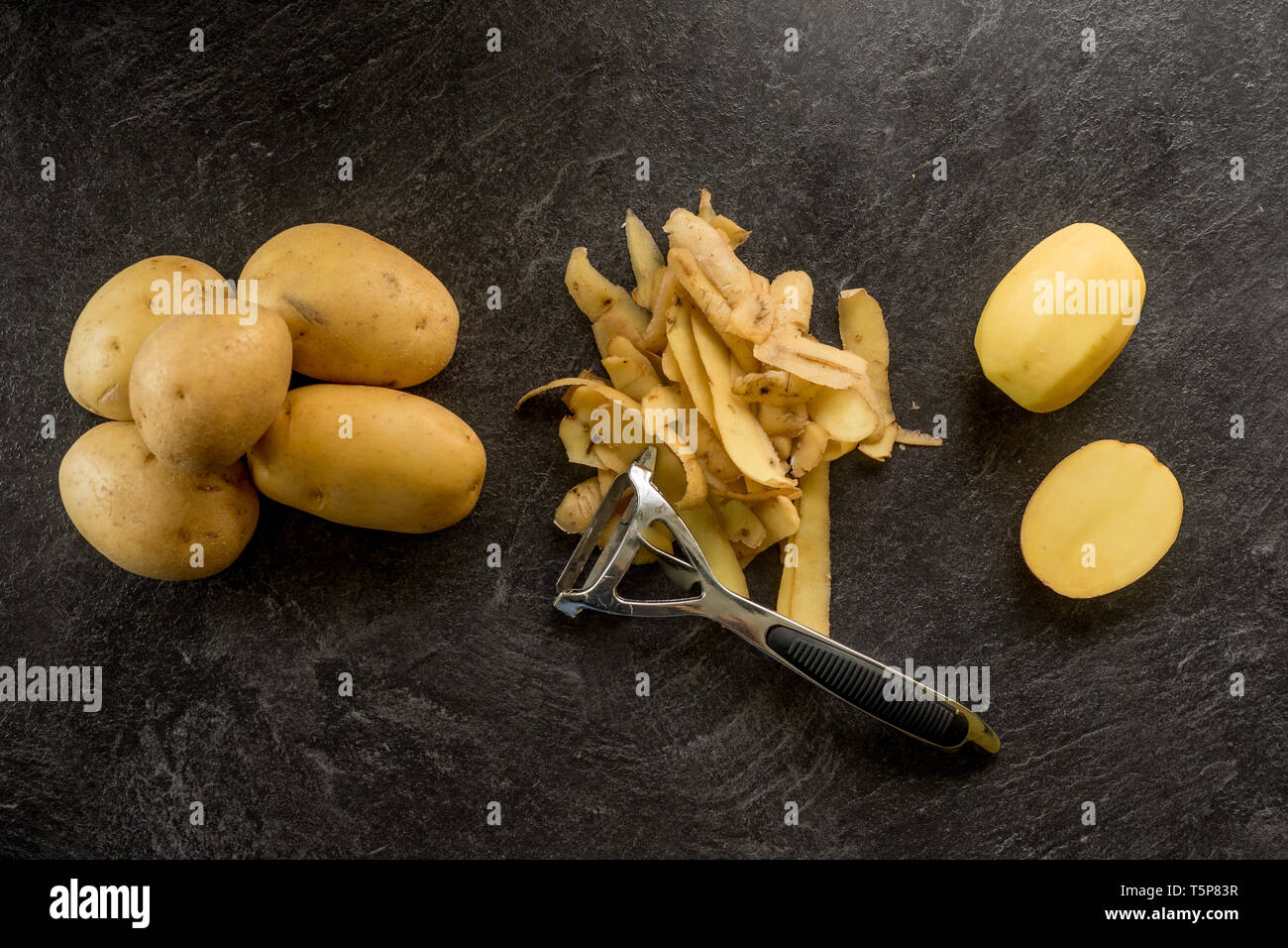 https://c8.alamy.com/comp/T5P83R/peeler-with-peeled-potatoes-and-their-skins-on-textured-black-background-photo-from-above-T5P83R.jpg