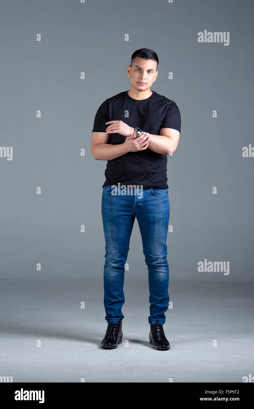 A studio shot of a young man in a black shirt, blue jeans and leather shoes  showing off his watch against a grey background Stock Photo - Alamy