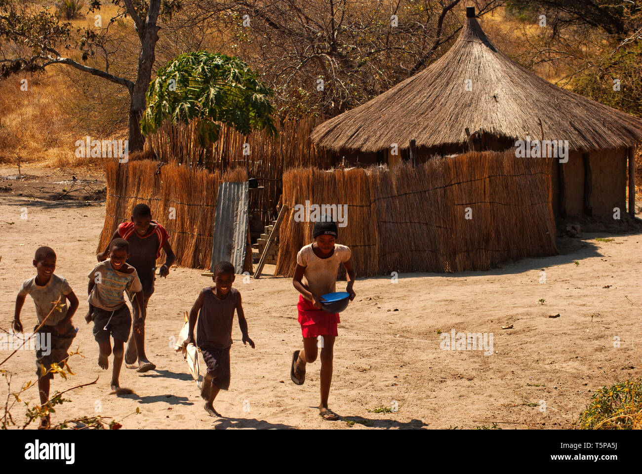 Young boys and girls running in front of their traditional grass hut, Caprivi Strip, Namibia Stock Photo